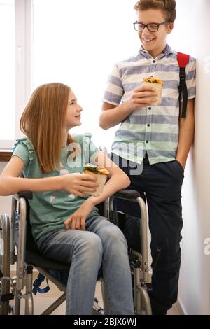 Une adolescente en fauteuil roulant avec des sandwichs pour les garçons dans le couloir scolaire Banque D'Images