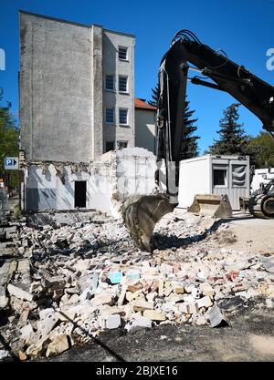 pelle hydraulique sur un site de démolition dans une zone urbaine. Un conteneur de site et des bois de conifères en arrière-plan et du caillou en premier plan. Banque D'Images