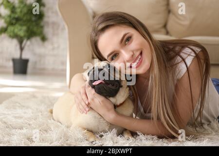 Belle jeune femme avec mignon pug chien à la maison Banque D'Images