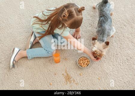 Une petite fille avec chien de manger des noix et de boire du jus tout en étant assis sur un tapis Banque D'Images