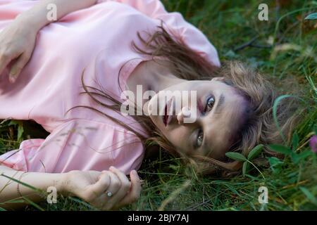 une fille zombie dans une robe rose se trouve sur l'herbe Banque D'Images