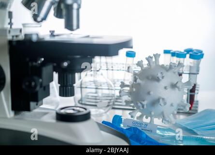 Microscope en laboratoire avec modèle de coronavirus et flacons d'essai Banque D'Images
