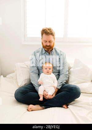 Père assis au lit avec bébé garçon (2-3 mois) Banque D'Images