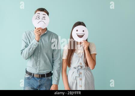 Deux visages se cacher derrière des feuilles de papier avec des émoticônes dessiné sur un fond de couleur Banque D'Images