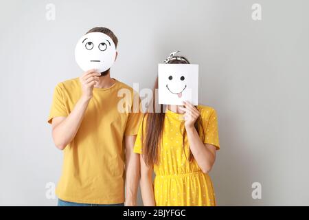 Deux visages se cacher derrière des feuilles de papier avec des émoticônes dessiné sur fond gris Banque D'Images