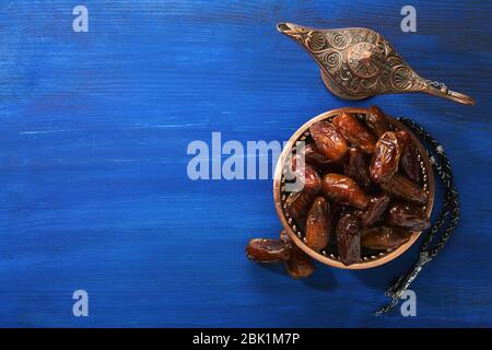 Plaque de bronze avec dattes, lampe aladdin et tasbih (misbaha) sur table en bois bleu foncé. Contexte du Ramadan. Pose plate. Banque D'Images