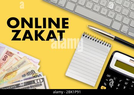 TEXTE ZAKAT (taxe islamique) EN LIGNE avec bloc-notes, calculatrice, clavier, billets multiples ou monnaie et stylo plume sur fond jaune. Zakat (islamique Banque D'Images