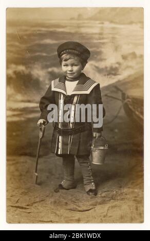 Début des années 1900 carte postale de bord de mer de jeune garçon portant un chapeau de victoire HMS, combinaison de marin, Eastbourne, Sussex, Angleterre, Royaume-Uni vers 1908 Banque D'Images