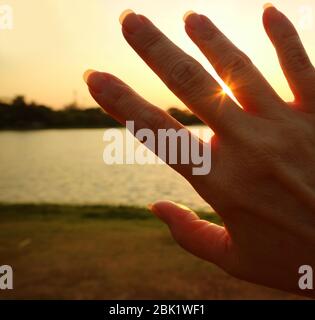 Lumière du soleil éblouissante qui brille par les doigts de la main de la femme Banque D'Images