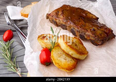 De délicieuses côtes levées au barbecue assaisonnées d'une sauce épicée au jus de viande, servies avec des pommes de terre cuites au four et du romarin frais. Banque D'Images