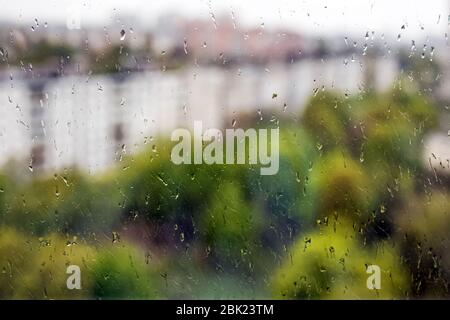 Gros plan sur les gouttes de pluie sur la fenêtre avec paysage de ville de printemps flou Banque D'Images
