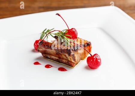 Côtes de porc grillées décorées de romarin et de cerise caramélisée servies sur une plaque blanche dans un restaurant Banque D'Images