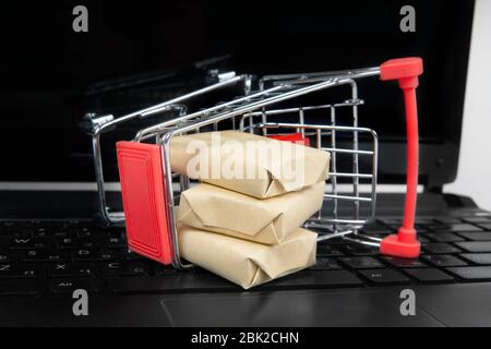 Un petit chariot de magasinage avec de petites boîtes de livraison se trouve sur un ordinateur portable noir. Achats en ligne. Gros plan, mise au point sélective. Banque D'Images