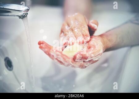 La personne se lave très soigneusement et diligemment les mains avec du savon sur un évier blanc dans lequel l'eau coule du robinet. Banque D'Images