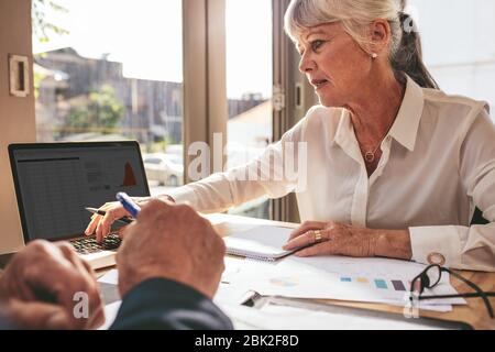 Femme d'affaires senior occupée à travailler sur un ordinateur portable avec un collègue assis à côté. hommes d'affaires travaillant sur des papiers à la table de café. Banque D'Images