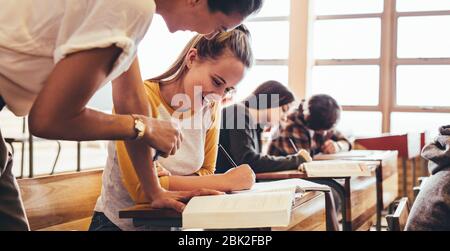 Étudiant participant à une conférence avec un enseignant aidant dans les études. Fille assise en classe étant aidée par un enseignant. Banque D'Images