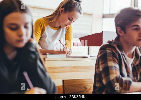 Une adolescente assise à son bureau dans la classe secondaire écrire dans un ordinateur portable. L'élève féminin prend des notes pendant la conférence à l'école. Banque D'Images