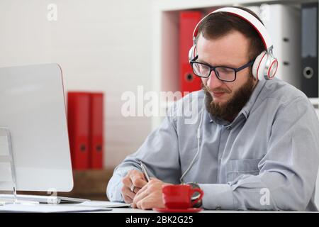 Un homme en casque d'écoute de la musique et apprend en ligne. Prend des notes sur un ordinateur portable et s'intéresse à l'appareil photo Banque D'Images