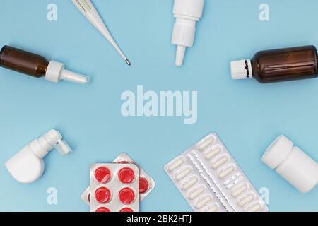 Divers médicaments, un thermomètre, pulvérise un nez bouché et une douleur dans la gorge sur fond bleu. Banque D'Images