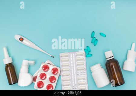 Divers médicaments, un thermomètre, pulvérise un nez bouché et une douleur dans la gorge sur fond bleu. Banque D'Images