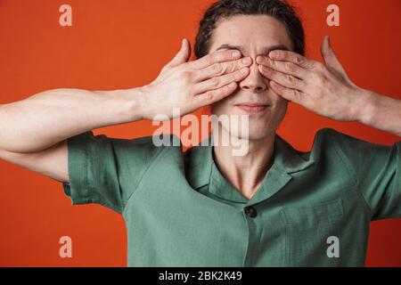 Image d'un jeune homme de handsome posant et couvrant ses yeux isolés sur fond orange Banque D'Images