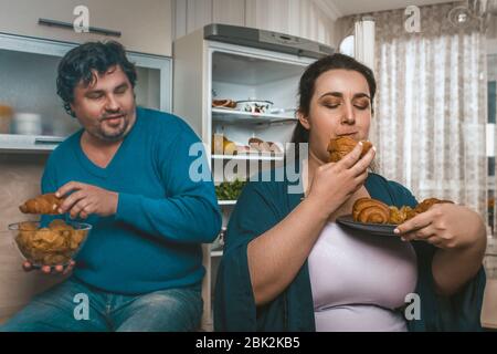 Le couple positif du corps surmange la nourriture malsaine avant le coucher Banque D'Images