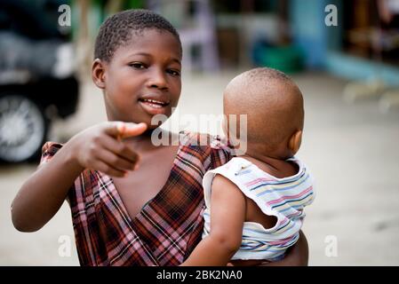 Abidjan, Côte d'Ivoire - 13 février 2018 : petite fille transportant son petit frère et pointant vers quelque chose. Banque D'Images