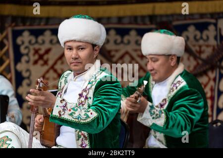 Portrait de deux hommes dans des vêtements traditionnels jouant un Dombra sur une scène au Kazakhstan Spring Festival à Victoria Embankment Gardens, Londres Banque D'Images