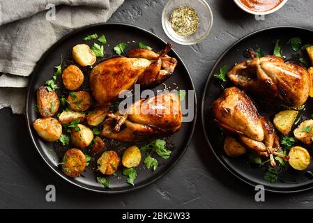 Carcasses de cailles grillées savoureuses avec pommes de terre cuites sur des assiettes sur fond de pierre noire. Vue sur le dessus, plat Banque D'Images