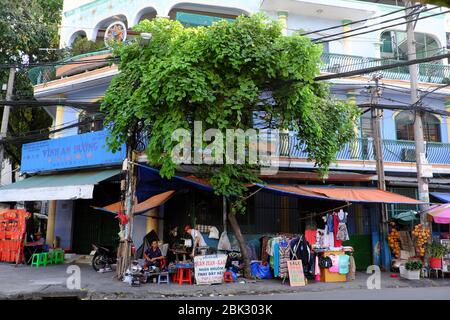 HO CHI MINH VILLE, VIET NAM, deux hommes vietnamiens travaillent à la boutique de tailleur extérieure, avec machine à coudre homme fixe vêtements sur le trottoir sous l'arbre Banque D'Images