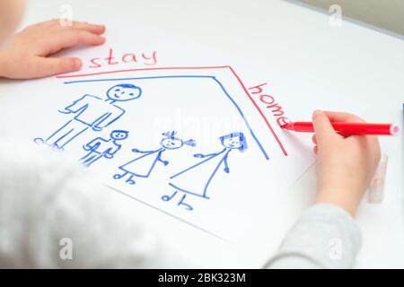 L'enfant écrit des mots rester à la maison avec la famille heureuse dessinée sur la feuille blanche de papier à la maison. Banque D'Images