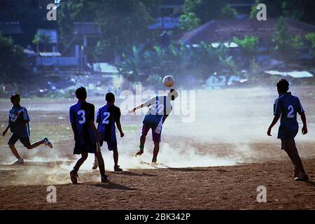 Les enfants jouent au football sur un terrain partiellement inondé, situé entre deux cimetières publics à Pondok Kelapa, Jakarta, Indonésie. Banque D'Images