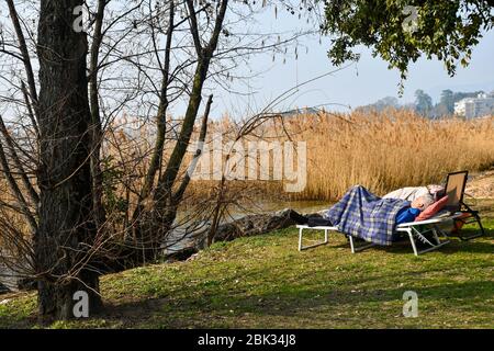 Un vieux gentleman prenant une sieste en plein air sur un lit de camp près du lac près d'un roseaux dans une journée d'hiver ensoleillée, lac de Garde, Bardolino, Vérone, Vénétie, Italie Banque D'Images