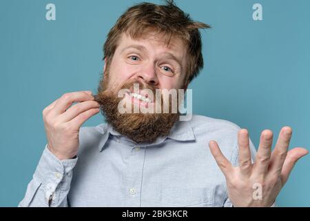 L'homme est mécontent de ses cheveux et de sa barbe chiches, il a besoin d'urgence d'un barbier. Concept de quarantaine pendant une épidémie virale. Banque D'Images