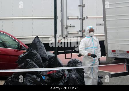 30 avril 2020, New York, New York, États-Unis: Cet homme, vêtu d'un hazmat, se dresse dans la rue entourée de camions. Derrière lui, de grands sacs à ordures noirs ont été entassés devant la maison funéraire Andrew T. Cleckley à Brooklyn où les corps non correctement entretenus sont enlevés. 60 cadavres ont été stockés dans 4 camions loués non repréenregistrés qui bordaient la rue des magasins à proximité. Les voisins ont signalé une odeur désagréable encore persistante et des liquides s'écoulaient des camions. Certains vestiges ont également été trouvés sur„ le plancher de la facilitation‚. Le salon funéraire a été submergé par les décès de COVID-19, en attendant des semaines de tapis Banque D'Images