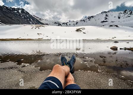 Les jambes de l'homme dans le suivi des chaussures et de la vue sur le lac glacier enneigé dans les montagnes Banque D'Images