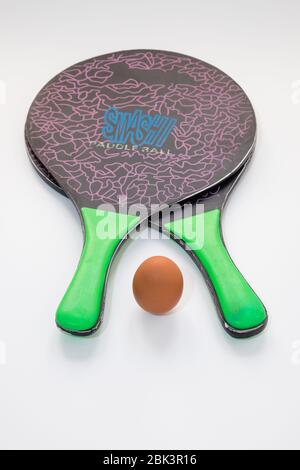 Deux raquettes de tennis de plage reposent sur un fond blanc, au centre il y a un œuf qui remplace le ballon, concept de nutrition sportive. Banque D'Images