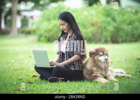 Belle jeune femme utilisant un ordinateur portable avec son petit chien dans un parc à l'extérieur. Portrait de style de vie. Banque D'Images