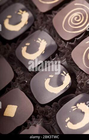 Truffes au chocolat noir et au lait de luxe. Assortiment de délicieux pralines au chocolat faites à la main à la suite. Marron foncé avec ornements dorés. Prise de vue en studio. Banque D'Images