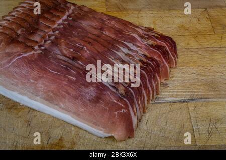 Jambon fumé italien en tranches sur un panneau de découpe en bois de gros plan. Banque D'Images