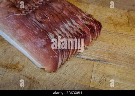 Jambon fumé italien en tranches sur un panneau de découpe en bois de gros plan. Banque D'Images