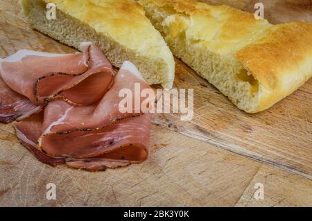 Jambon fumé italien en tranches avec du pain focaccia sur un tableau de découpe en bois près. Banque D'Images