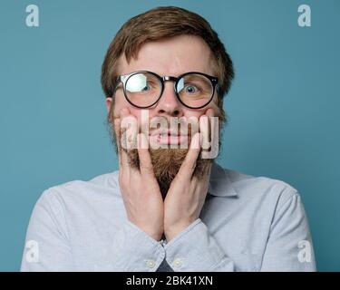 Homme drôle avec des lunettes mettre les doigts dans sa barbe en forme de poils. Il est bouleversé parce qu'il ne peut pas visiter le barbershop en raison de la quarantaine. Banque D'Images