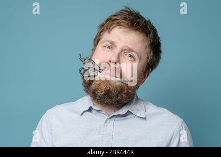 Homme malcontent et tiraillé avec des ciseaux dans sa bouche à l'hystérie, il n'était pas dans le barbershop depuis longtemps. Quarantaine Banque D'Images