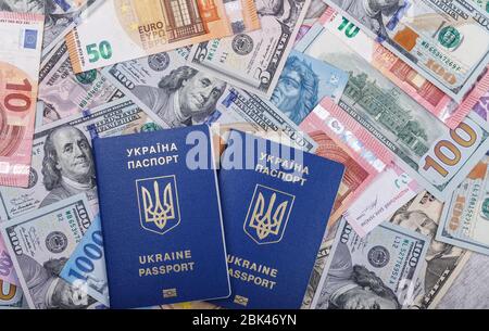 Deux passeports biométriques ukrainiens se trouvent sur un fond de devises provenant de différents pays du monde, euros, dollars, hryvnias, forints. Le Banque D'Images