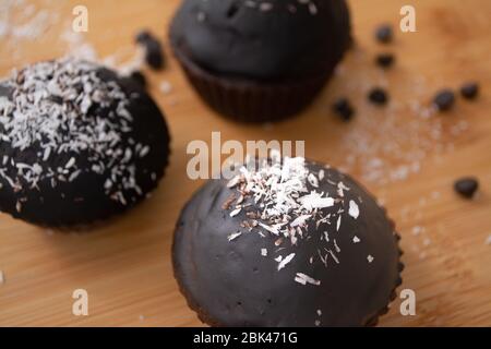 Chocolat glacé chocolat cacao gâteau muffins avec flocons de noix de coco en rangées sur un panier de refroidissement en métal Banque D'Images