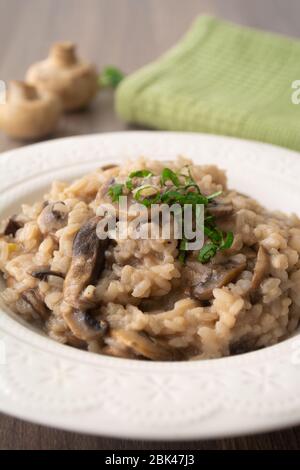 Risotto italien classique aux champignons vegan, à base de riz à l'arborio, de champignons, d'oignons et d'ail, garni de rubans de basilic sur une surface rustique en bois avec de l'humour Banque D'Images