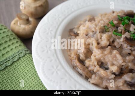 Risotto italien classique aux champignons vegan, à base de riz à l'arborio, de champignons, d'oignons et d'ail, garni de rubans de basilic sur une surface rustique en bois avec de l'humour Banque D'Images