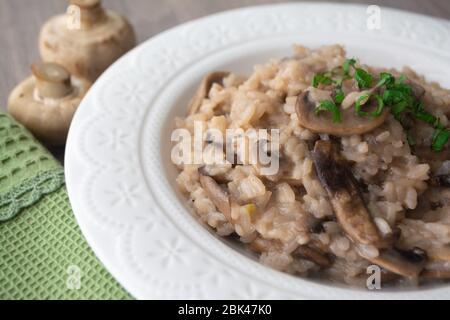 Risotto italien classique aux champignons vegan, à base de riz à l'arborio, de champignons, d'oignons et d'ail, garni de rubans de basilic sur une surface rustique en bois avec de l'humour Banque D'Images