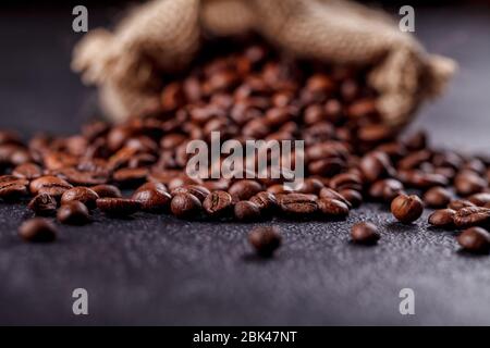 Grains de café aromatiques rôtis saupoudrés d'un sac en toile sur une surface sombre. Le concept de la tradition du café du matin. Vue latérale supérieure Banque D'Images